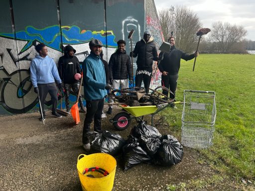 A group of people standing with garbage bags and tools near a grassy area.